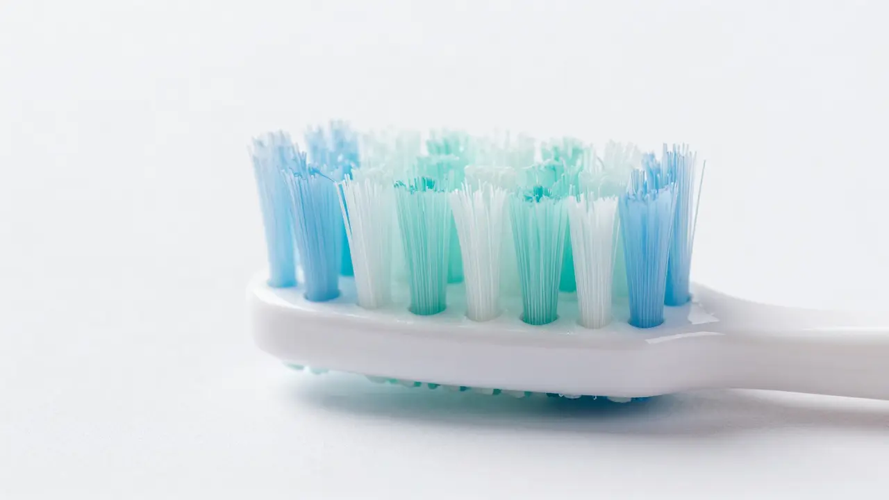 Detailní makro záběr jemných štětin zubního kartáčku šetrně čistících bílý zub.